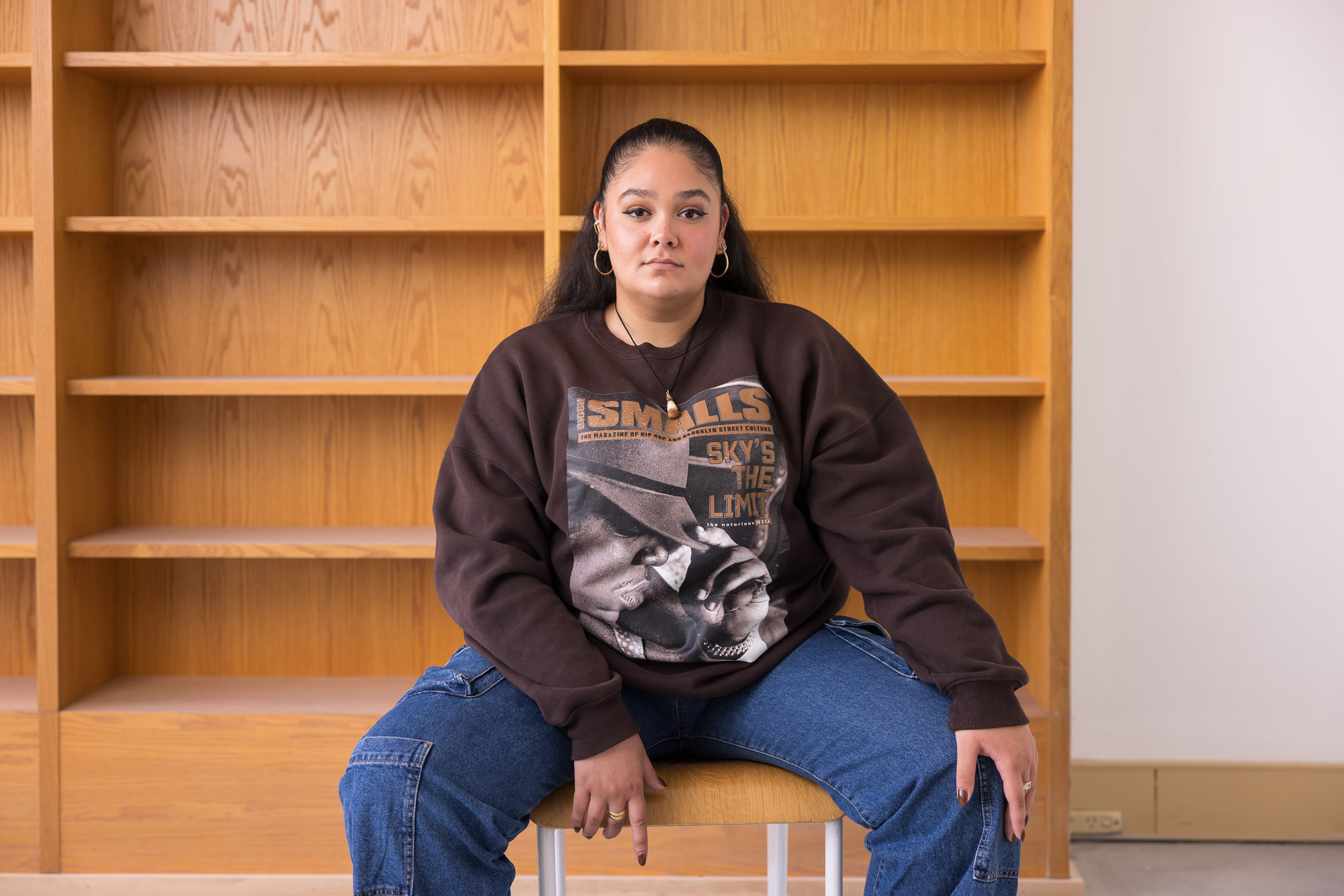 A woman sitting a room backed by a bookshelf