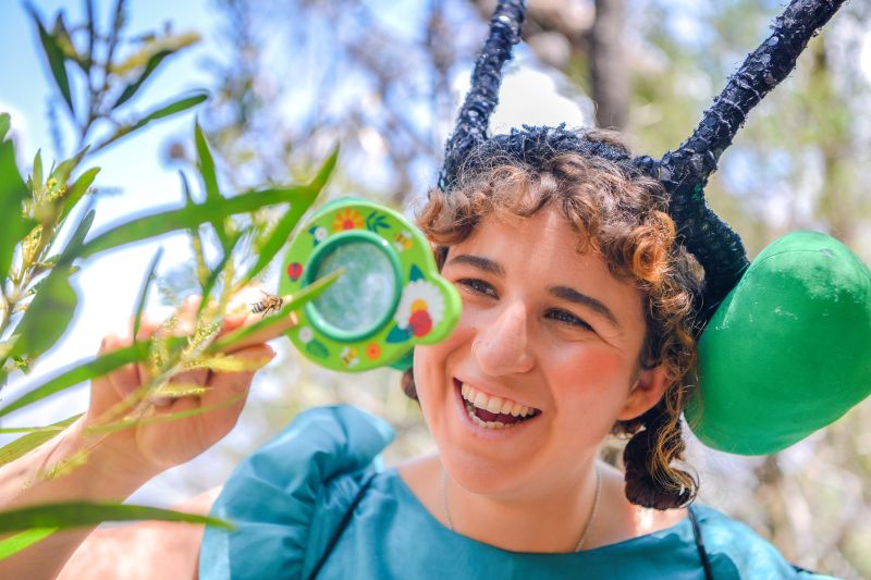 Woman smiling and looking through magnifying glass at a bee on a plant