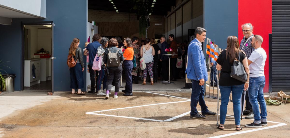 A group of people gathered around the entrance of large building with an open roller door