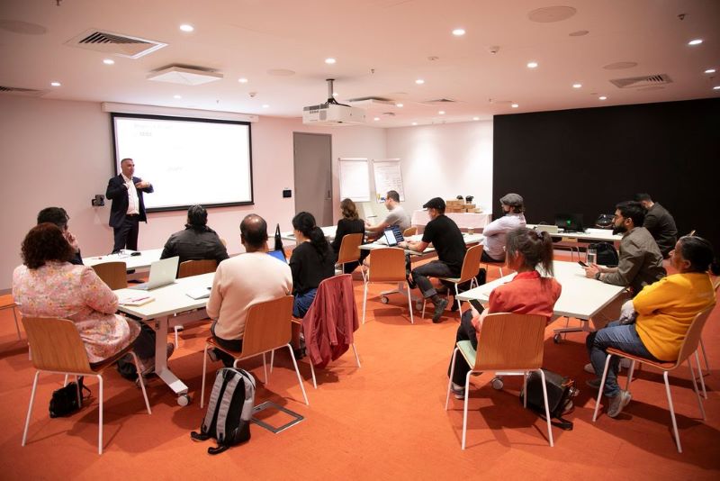 Man in front of class attended by women and men 